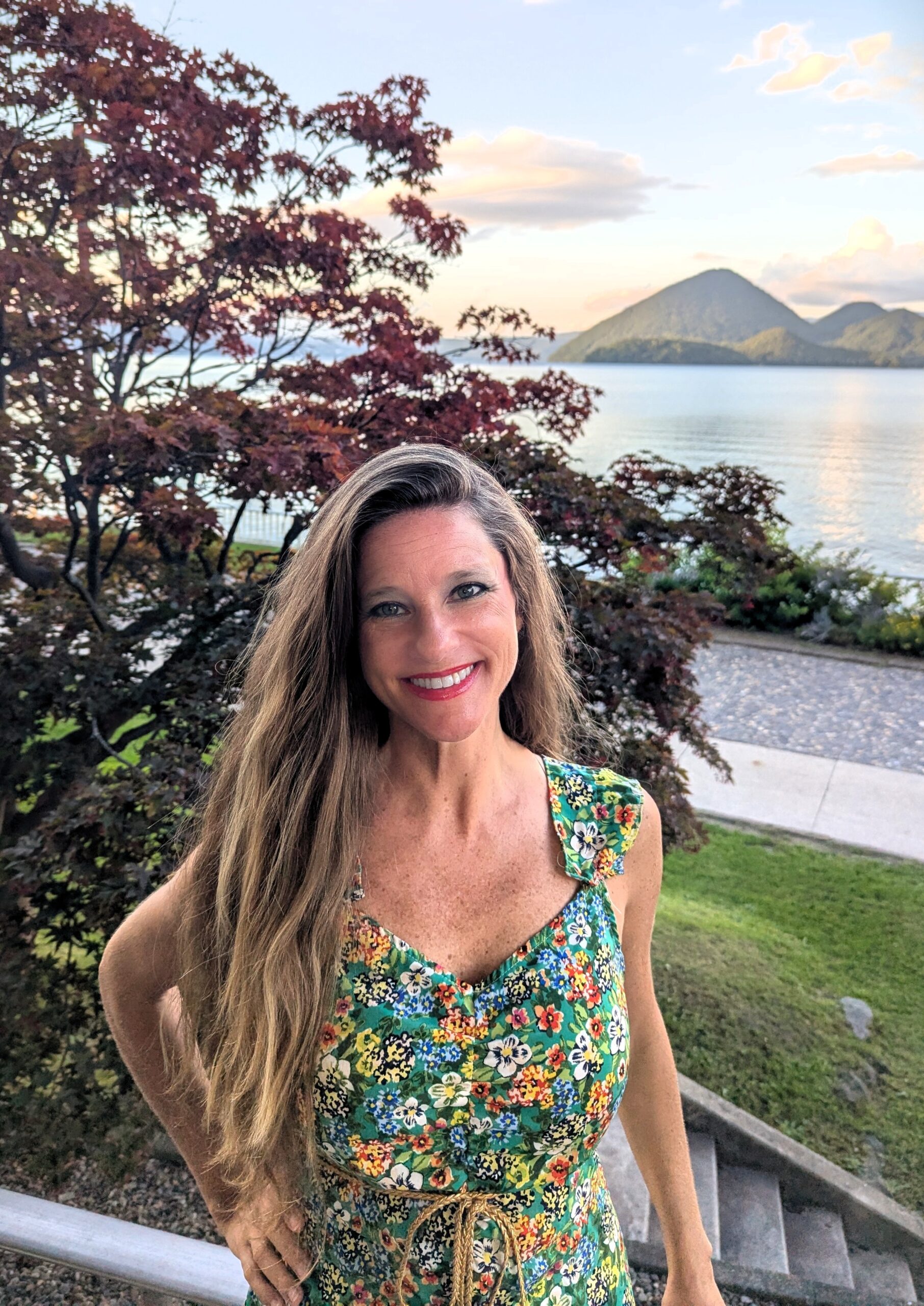 Woman in floral dress with lake and mountain view. Travel fashion, outdoor lifestyle.